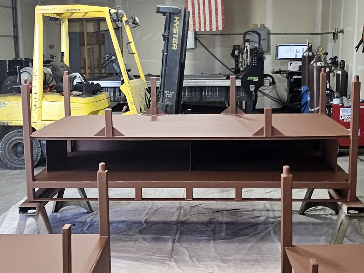 Inside the shop: forklift, the CNC plasma table and a set of primed steel stands.